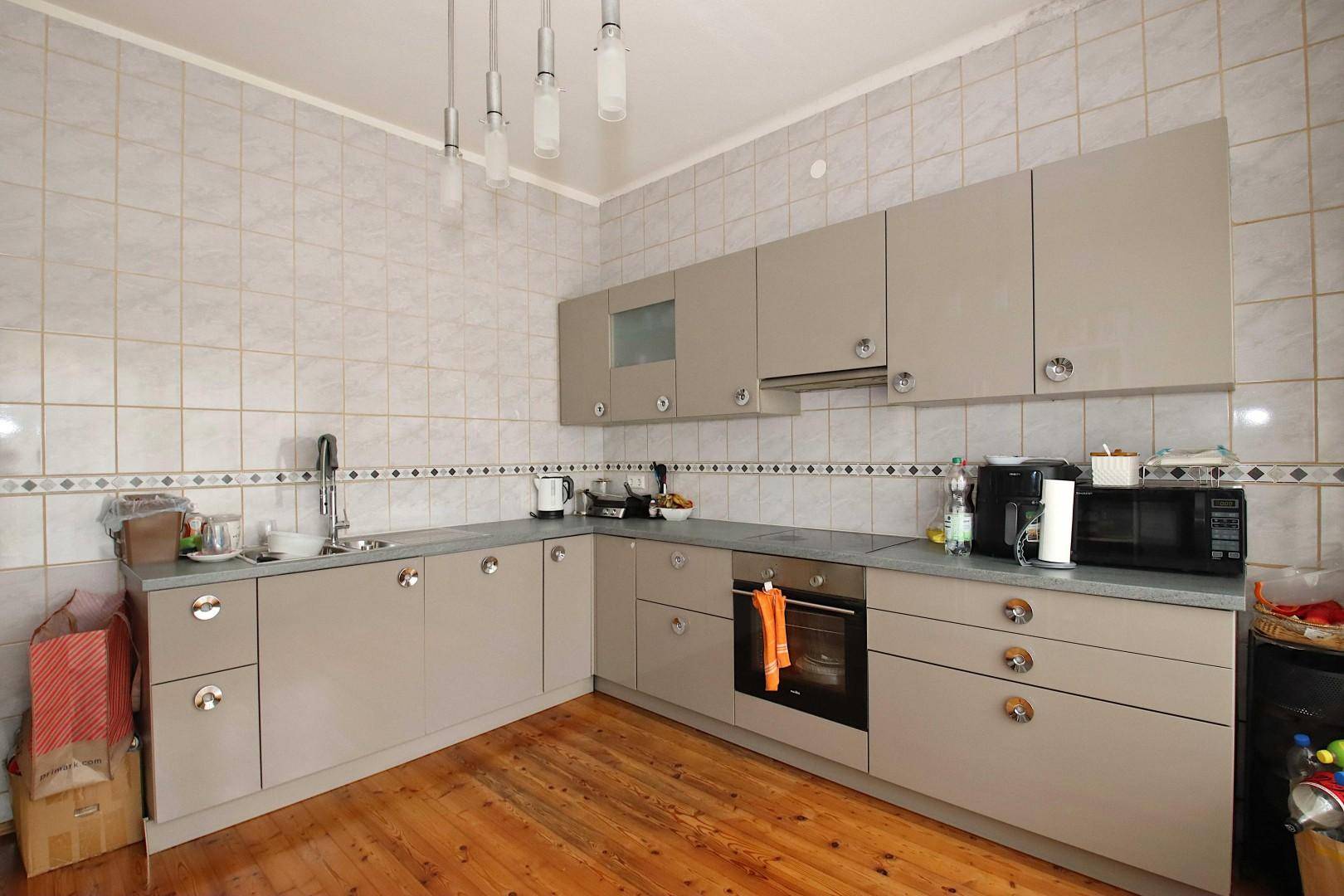 Funktionale Küche mit beigen Schränken, Fliesenwand und Holzboden.