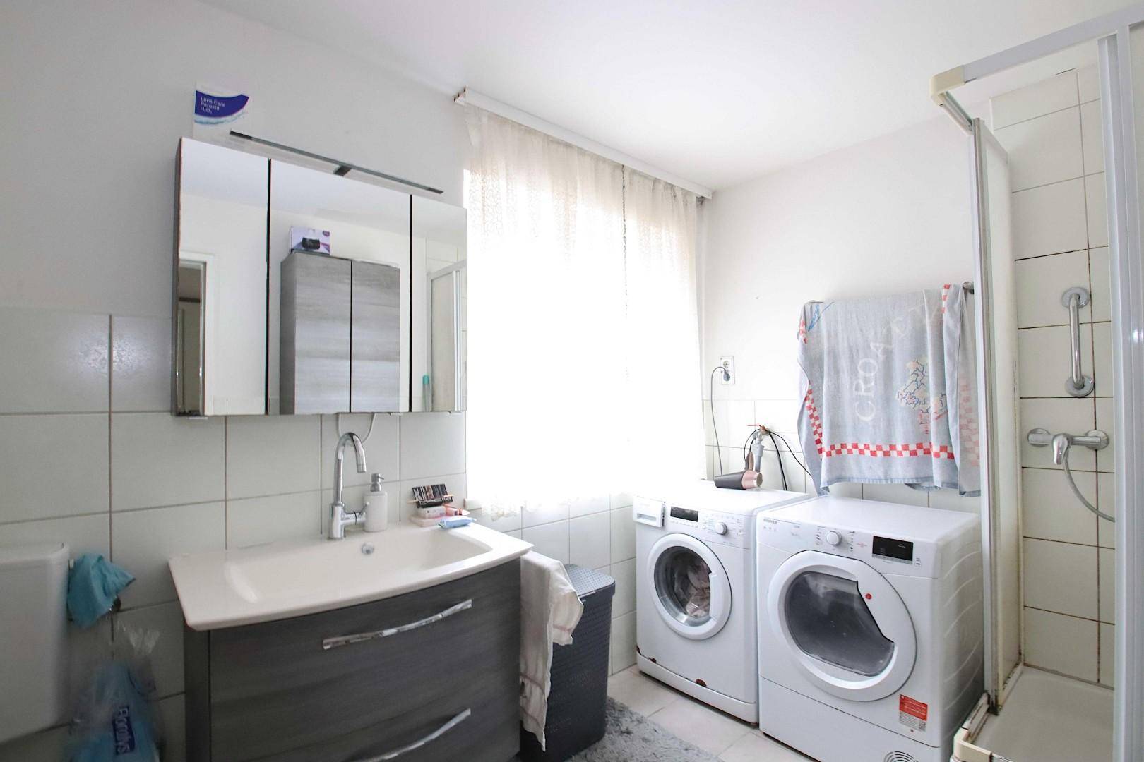 Modernes Badezimmer mit Waschbecken, Dusche, Waschmaschine und Trockner.