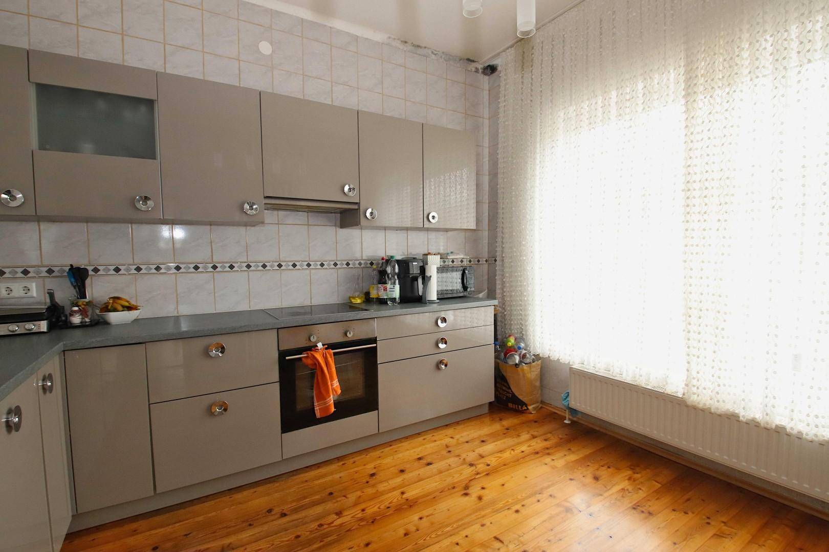 Helle Küche mit beigen Schränken, Holzboden und einem Fenster mit Vorhängen.