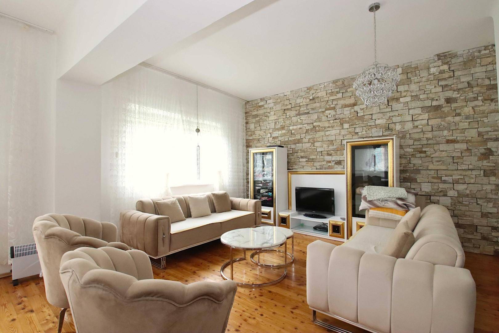 Helles Wohnzimmer mit beigen Sofas, Holzboden und einer dekorativen Steinwand.