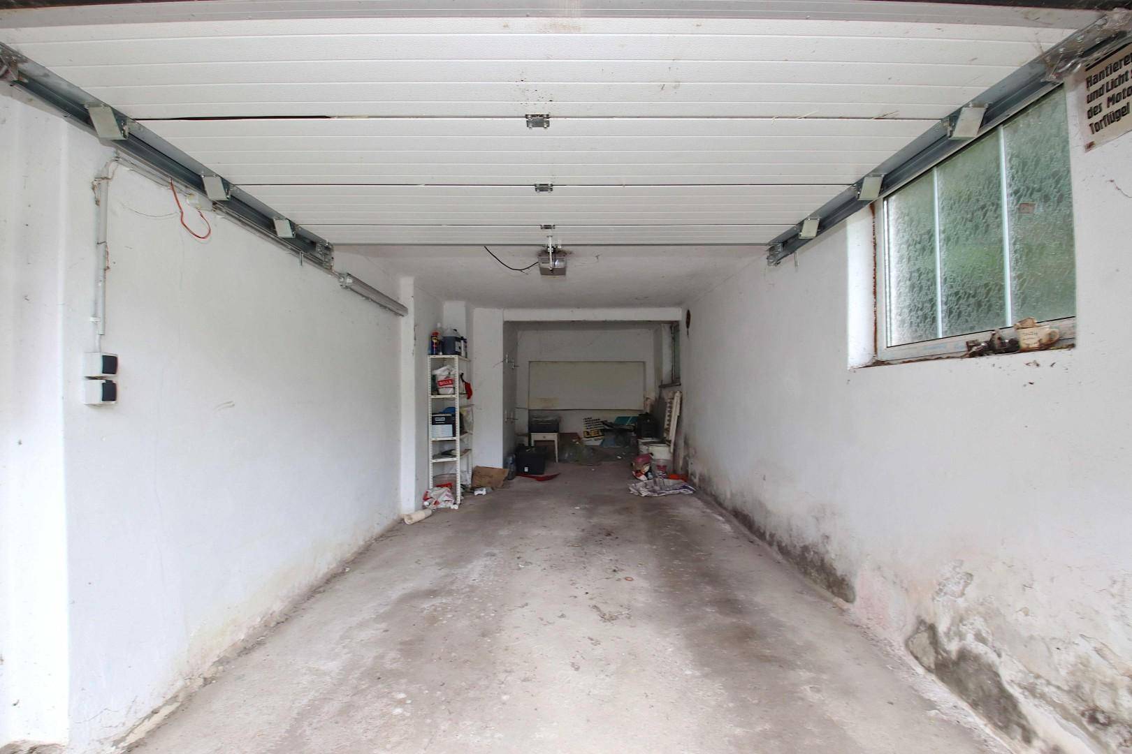 Lange, schmale Garage mit Betonboden und einem Fenster.