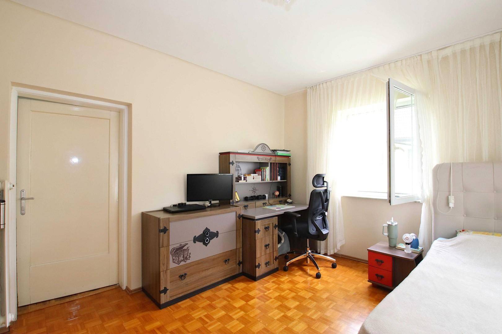 Schlafzimmer mit Holzboden, Schreibtisch und einer Tür zum Flur.