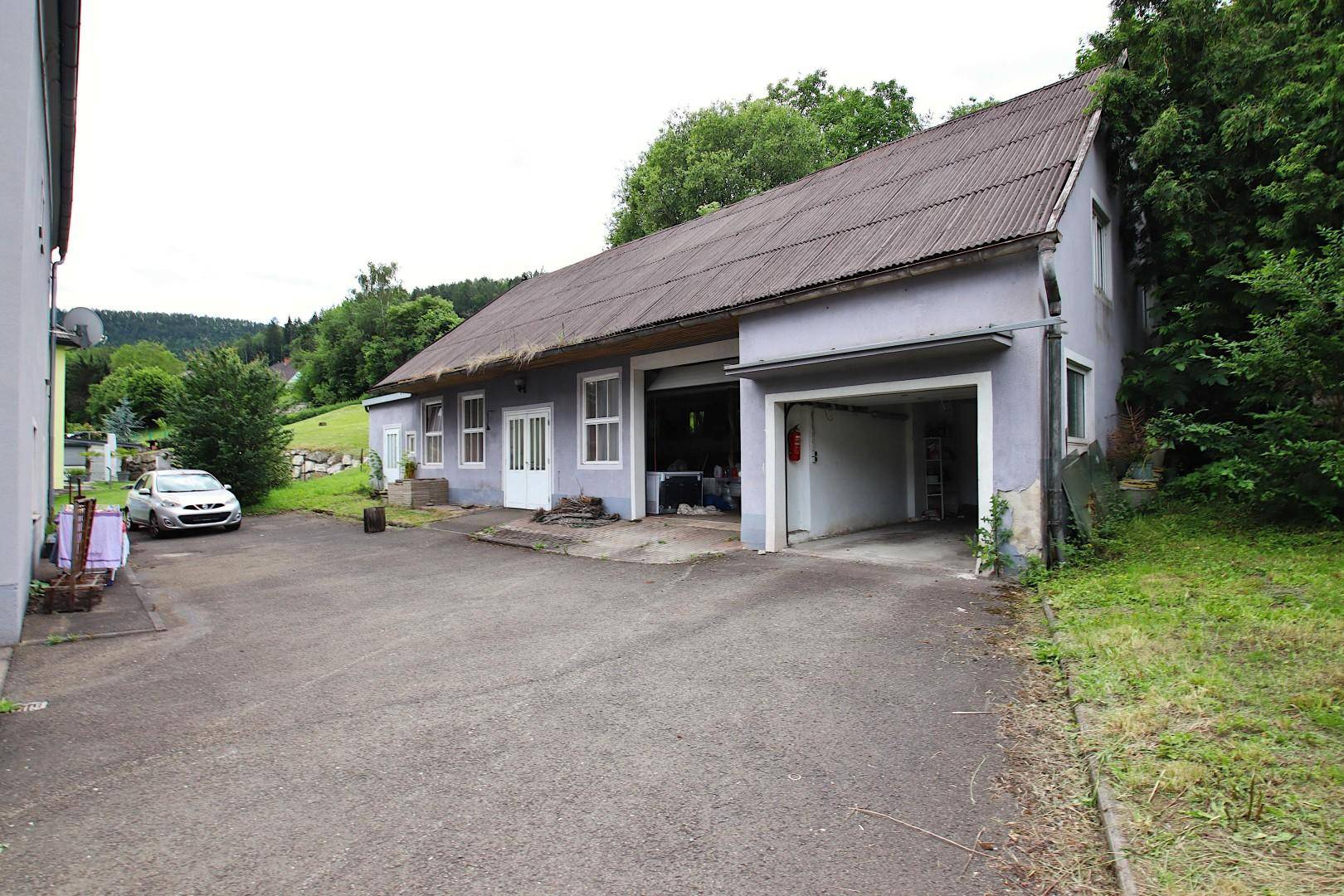 Seitenansicht des Nebengebäudes mit Garageneinfahrt und ländlicher Umgebung.