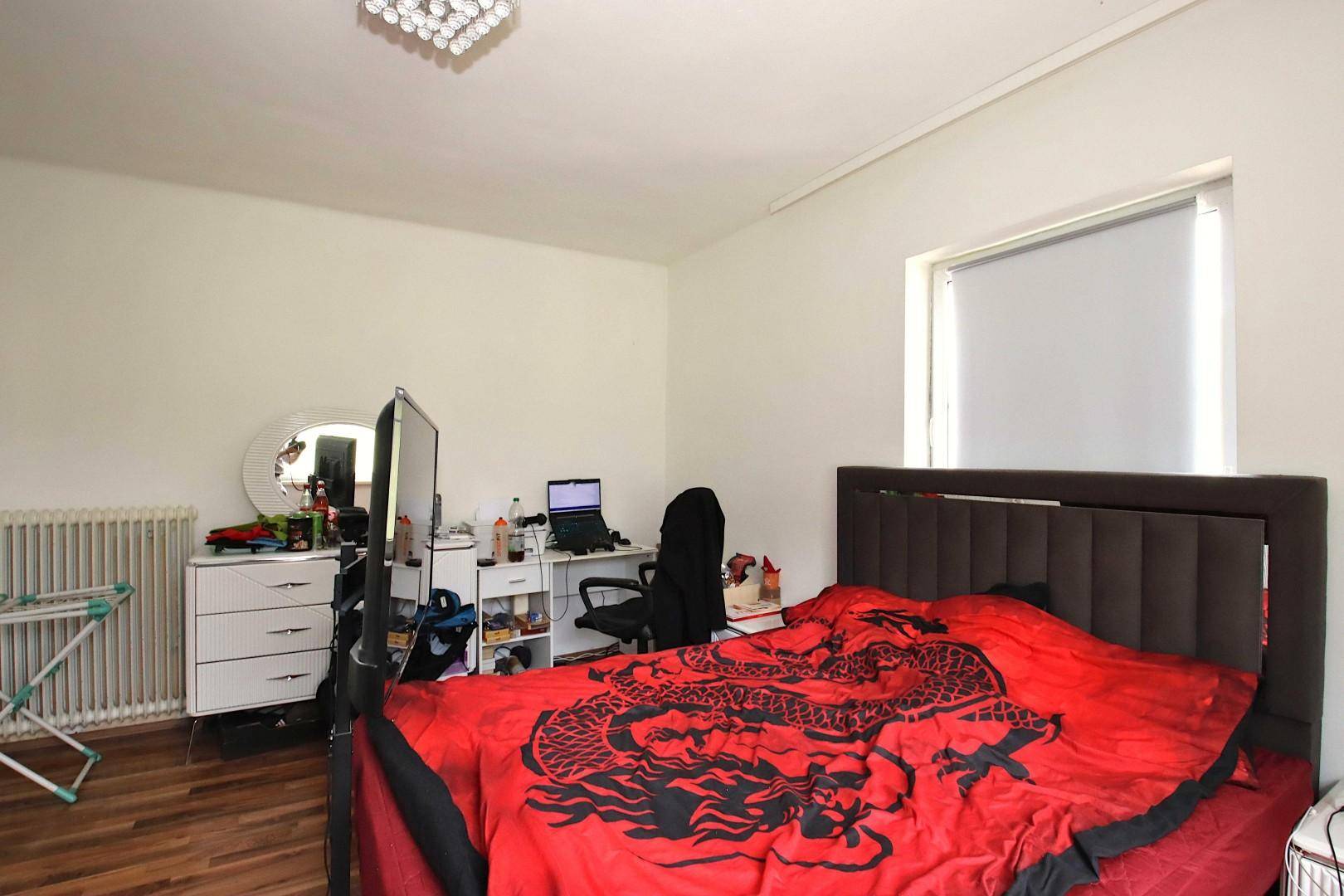 Schlafzimmer mit großem Bett, Schreibtisch und Fenster, dekoriert mit roter Bettwäsche.