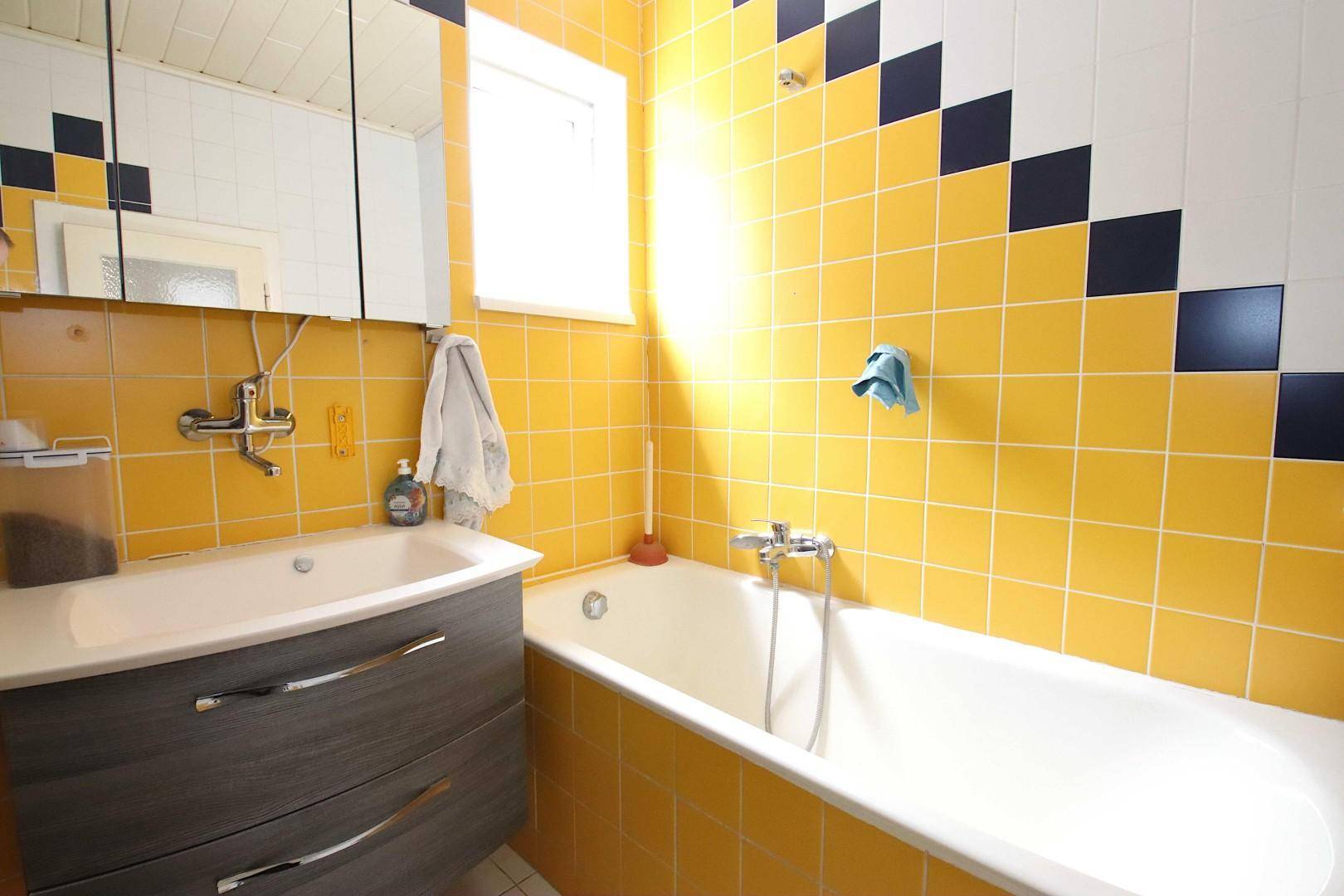 Badezimmer mit gelben Fliesen, Badewanne und Waschbecken mit Spiegelschrank.