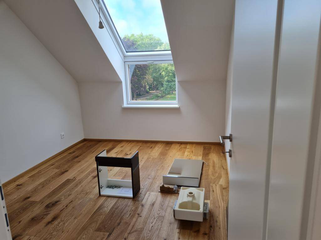 Dachgeschosszimmer mit Holzboden, Dachschräge und Blick ins Grüne durch das Fenster.