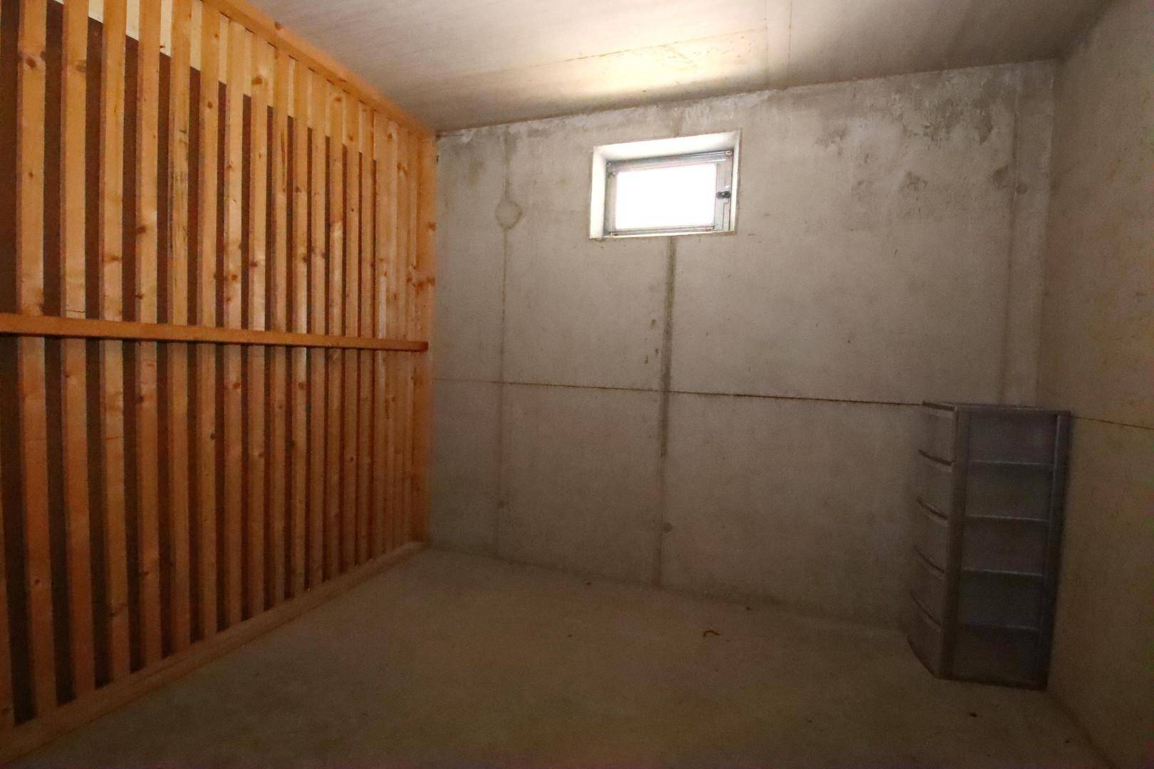 Kellerabteil mit Holzlattenwänden und kleinem Fenster, ideal als Abstellraum.