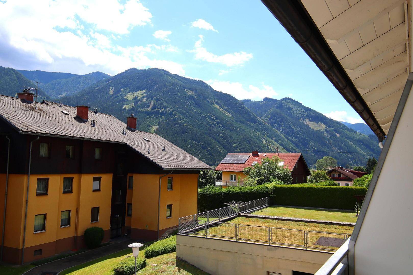 Weitläufiger Blick vom Balkon auf die grüne Berglandschaft und benachbarte Gebäude.