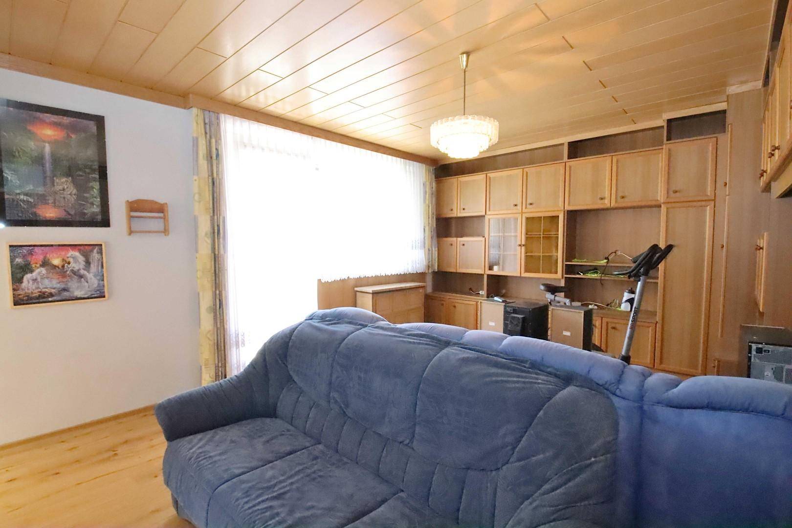 Geräumiges Wohnzimmer mit viel Tageslicht, blauer Couch und maßgefertigten Holzschränken.