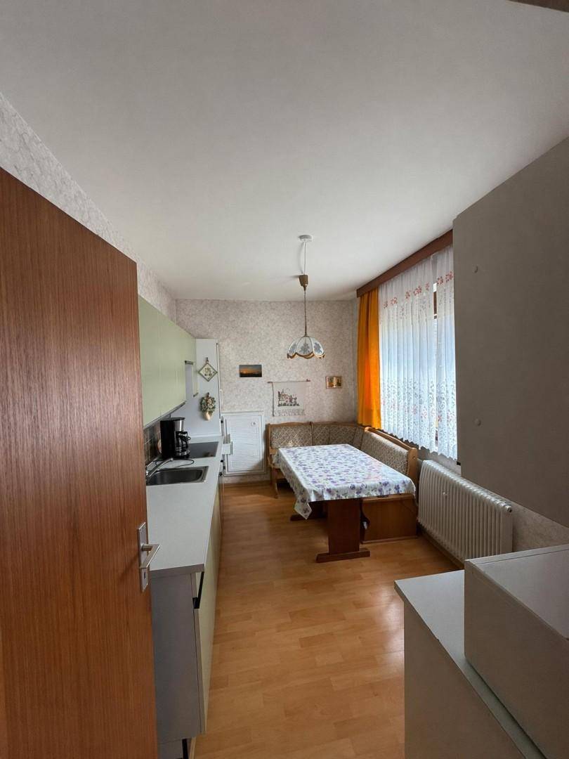 Gemütliche Küche mit heller Einbauküche, Essbereich und Holzfußboden, gut beleuchtet durch das Fenster.