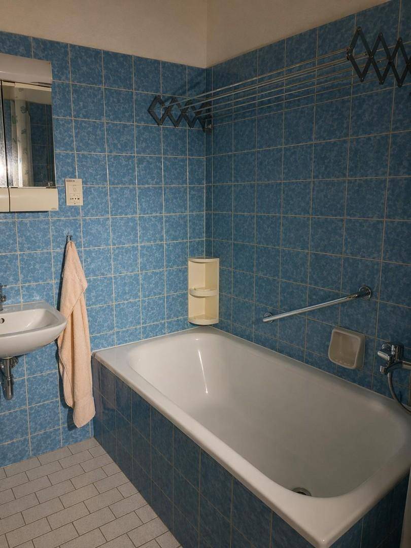 Badezimmer mit blauen Fliesen, Badewanne, kleinem Waschbecken und Spiegelschrank.