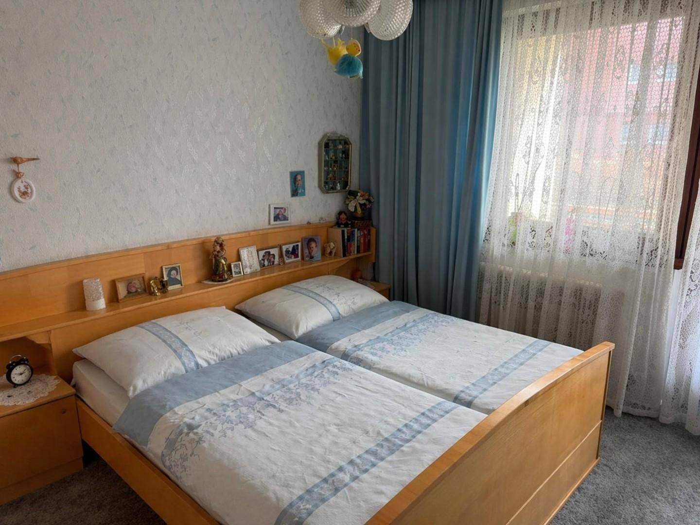 Schlafzimmer mit zwei Einzelbetten, Holzmöbeln und Teppichboden, hell durch das Fenster.