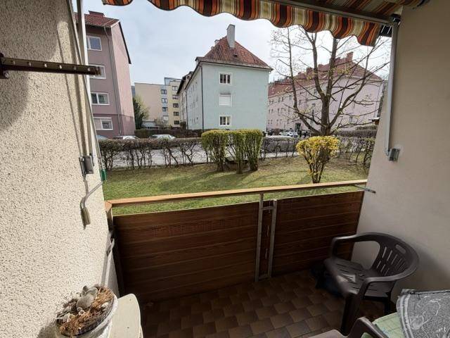 Kleiner Balkon mit Markise, Fliesenboden und Blick auf die umliegenden Gebäude und Grünflächen.