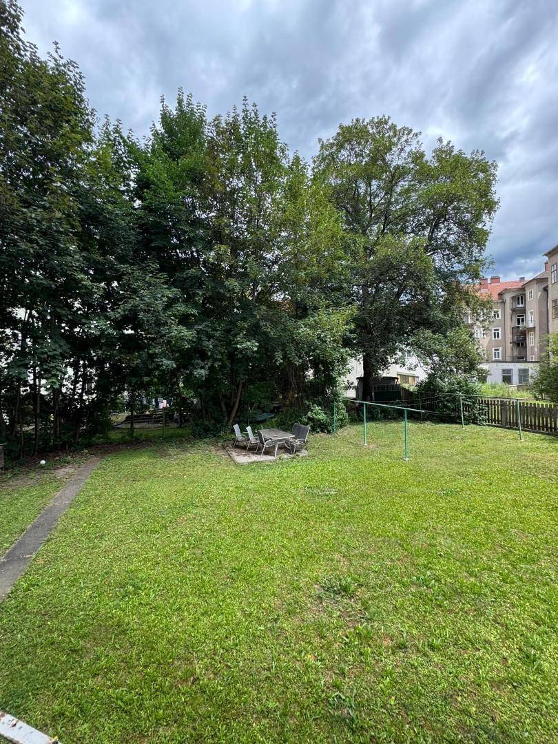 Großer grüner Garten mit Rasenfläche, Bäumen und einer kleinen Sitzecke im Freien.