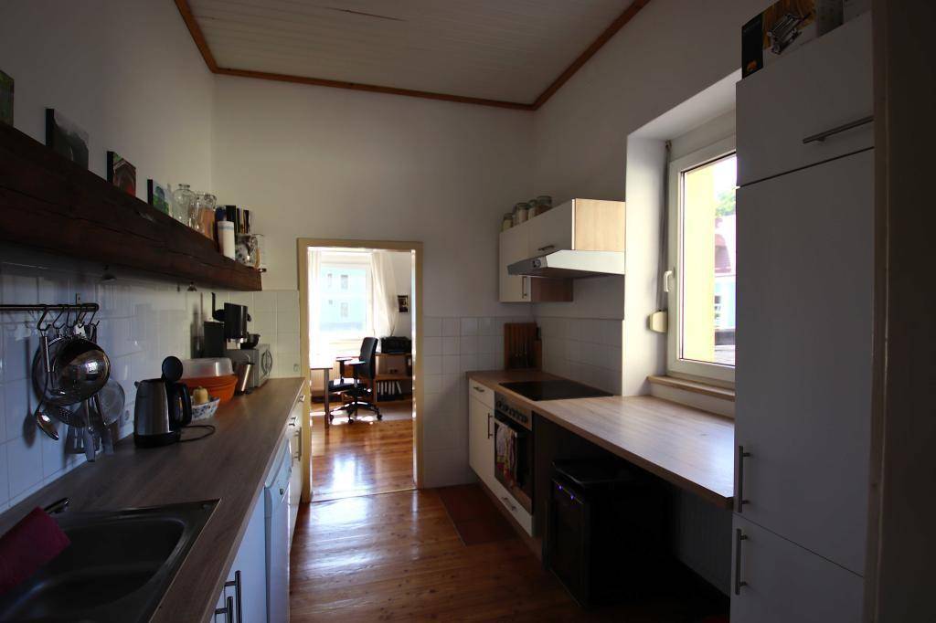Funktionale Küche mit Holz-Arbeitsplatten, weißen Schränken und Blick durch eine Tür in einen weiteren Raum.