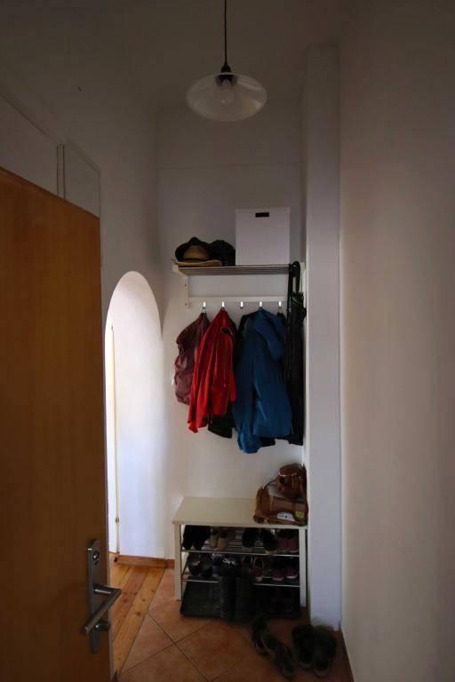 Eingangsbereich mit Garderobe, Schuhregal und einem Bogen, der zu einem weiteren Raum mit Holzfußboden führt.
