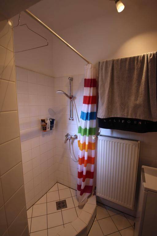 Eckdusche mit bunten Vorhängen in einem gefliesten Badezimmer, ausgestattet mit einem Heizkörper.