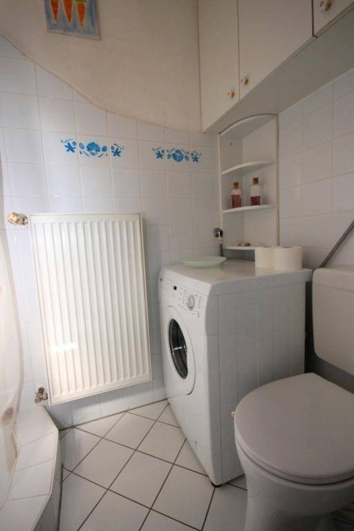 Badezimmer mit Toilette, Waschmaschine und Heizkörper, komplett gefliest mit blauen Dekorationsakzenten.