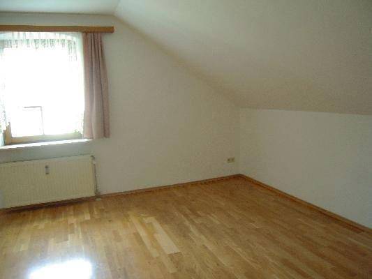 Leerer Raum im Dachgeschoss mit Holzfußboden, Fenster und schräger Decke.