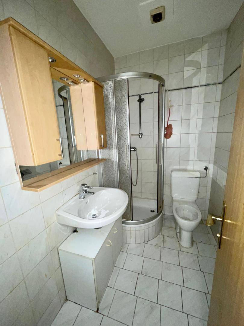 Kleines Badezimmer mit weißen Fliesen, Duschkabine, Waschbecken und WC.