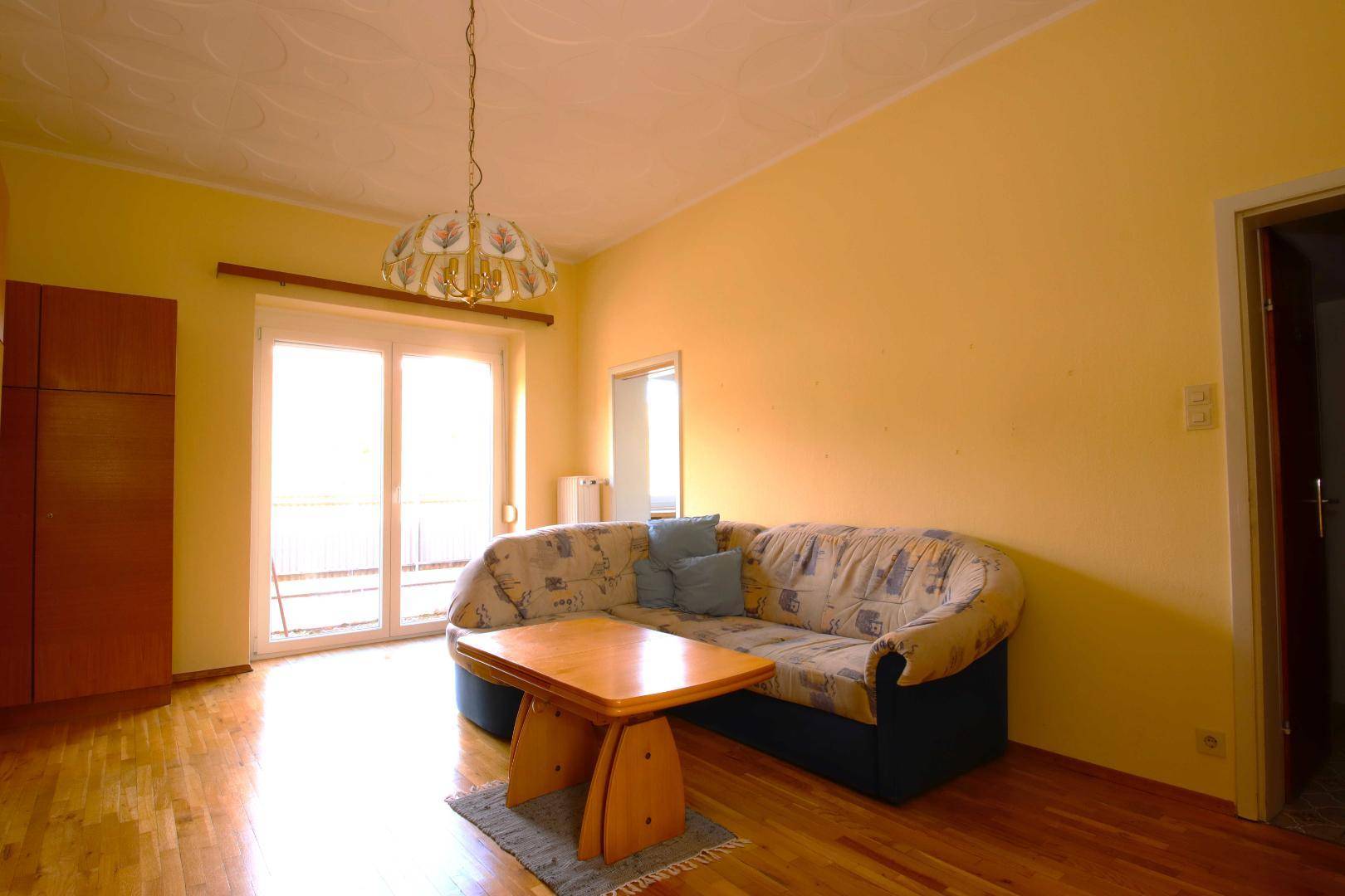 Helles Wohnzimmer mit gelben Wänden, Holzboden, Sofa und Zugang zu einem Balkon.
