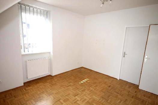 Leerer Raum mit weißen Wänden, Parkettboden, Fenster mit Heizkörper und zwei weißen Türen.
