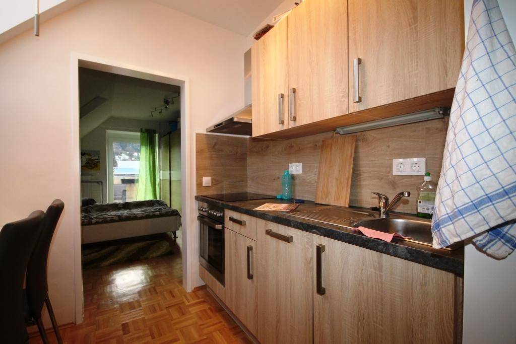 Kleine Küchenzeile mit Holzschränken und dunkler Arbeitsplatte, angrenzend an ein Schlafzimmer.