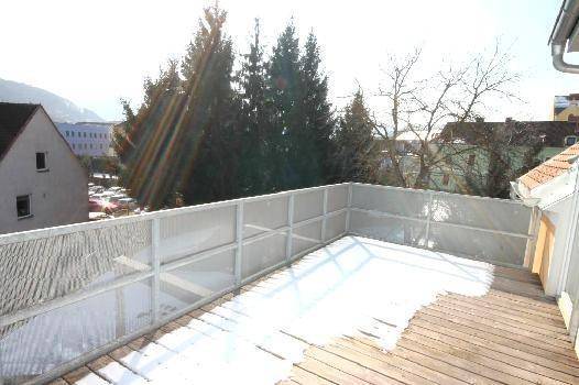 Holzterrasse mit Schnee bedeckt, umgeben von einem Metallgeländer, mit Blick auf Bäume und Gebäude.