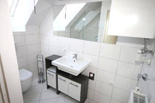 Modernes Badezimmer mit weißen Fliesen, Waschtisch, Toilette und Dachschräge mit Oberlicht.