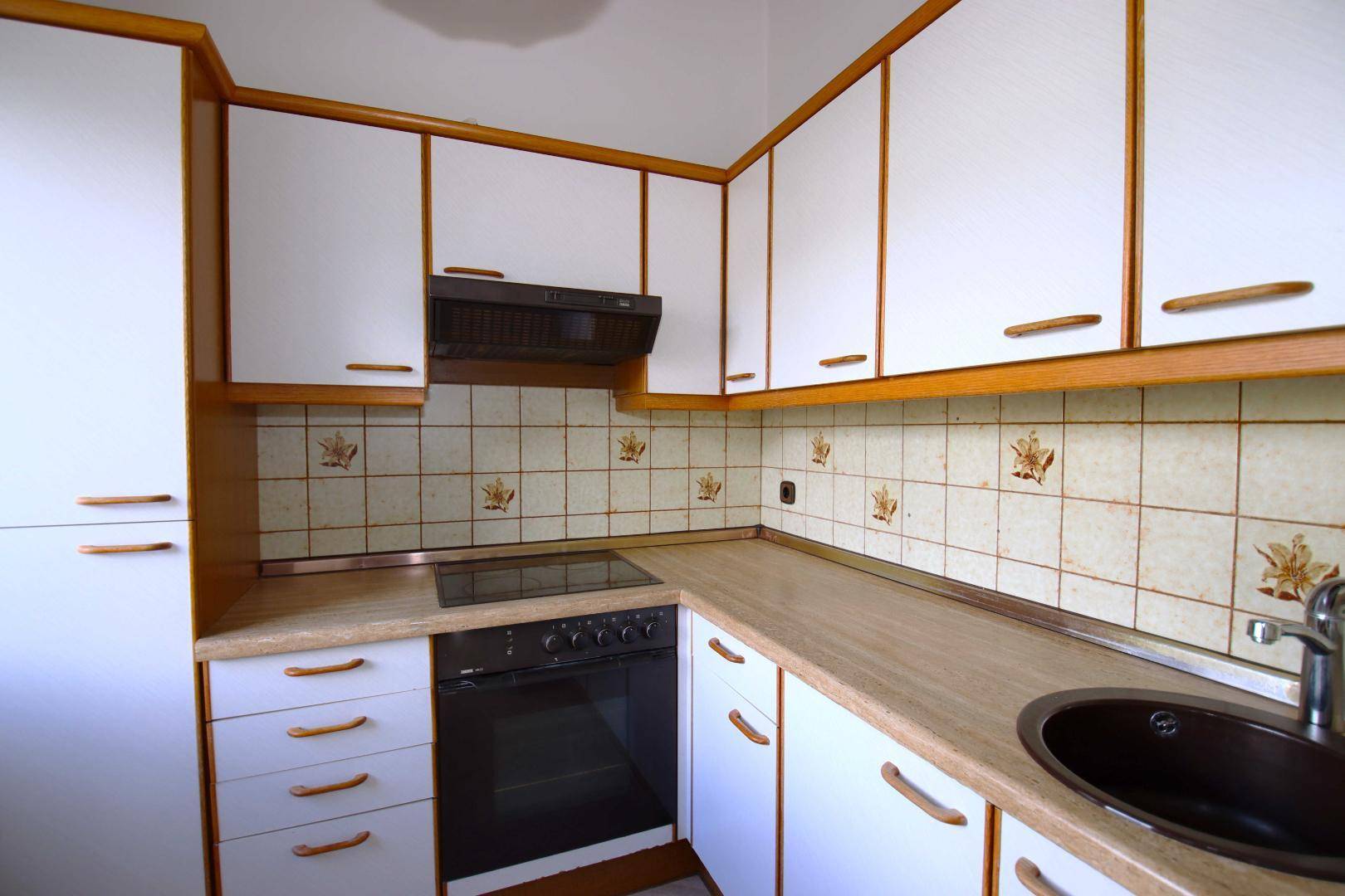 Klassische Küche mit weißen Schränken, Holzakzenten, Fliesenrückwand und Einbaugeräten.