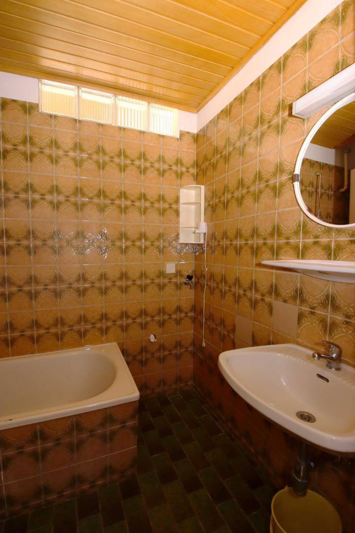 Badezimmer mit gemusterten Fliesen, Badewanne, Waschbecken und einer Holzdecke im Retro-Stil.