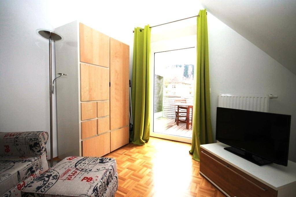 Wohnzimmer mit Parkettboden, Kleiderschrank, Sofa und Balkonzugang unter einer Dachschräge.