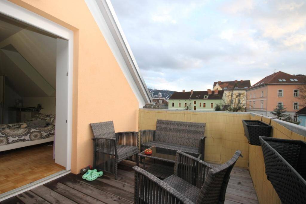 Balkon mit Korbmöbeln und Blick auf die umliegenden Gebäude unter einem bewölkten Himmel.
