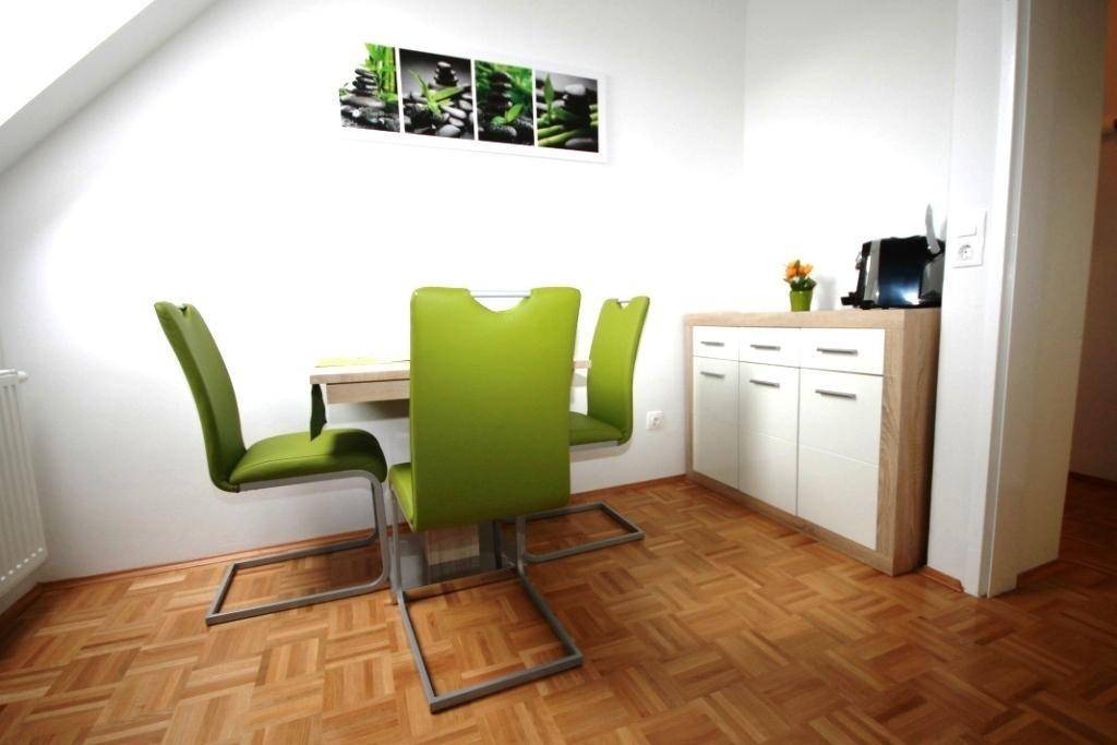 Essbereich mit modernem Tisch und vier grünen Stühlen, ergänzt durch ein weißes Sideboard.