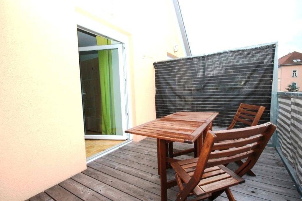 Balkon mit hölzernen Gartenmöbeln und einem Sichtschutz, ideal für entspannte Stunden im Freien.