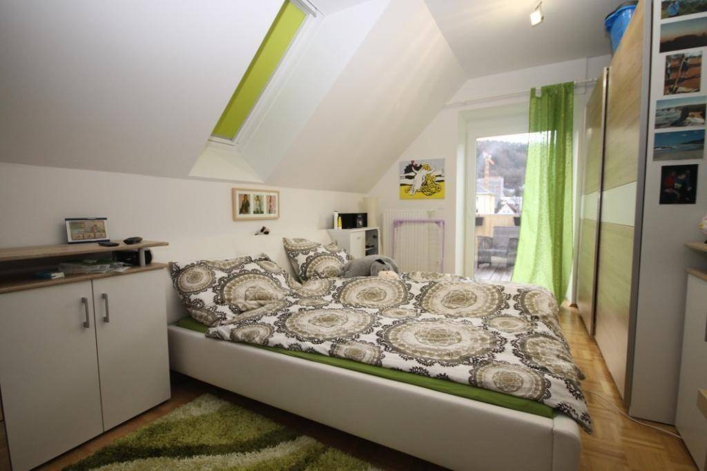 Schlafzimmer mit Bett, Kleiderschrank und Zugang zu einem Balkon, unter einer Dachschräge.