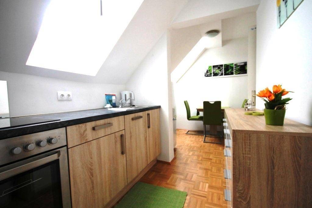 Küchenzeile mit Holzschränken und dunkler Arbeitsplatte, offen zum Essbereich, unter einem Dachfenster.
