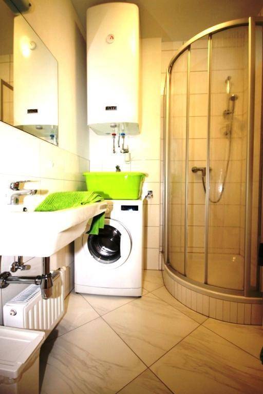 Funktionales Badezimmer mit Duschkabine, Waschbecken, Waschmaschine und Warmwasserboiler.