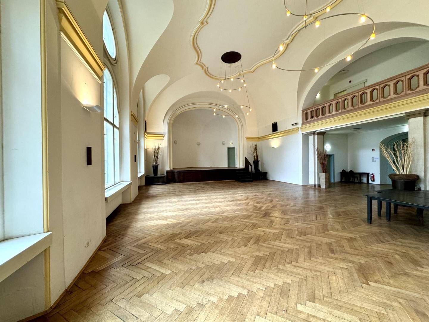Weitläufiger Festsaal mit beeindruckenden Gewölbedecken, Fischgrätparkett und Zugang zu einem oberen Bereich.