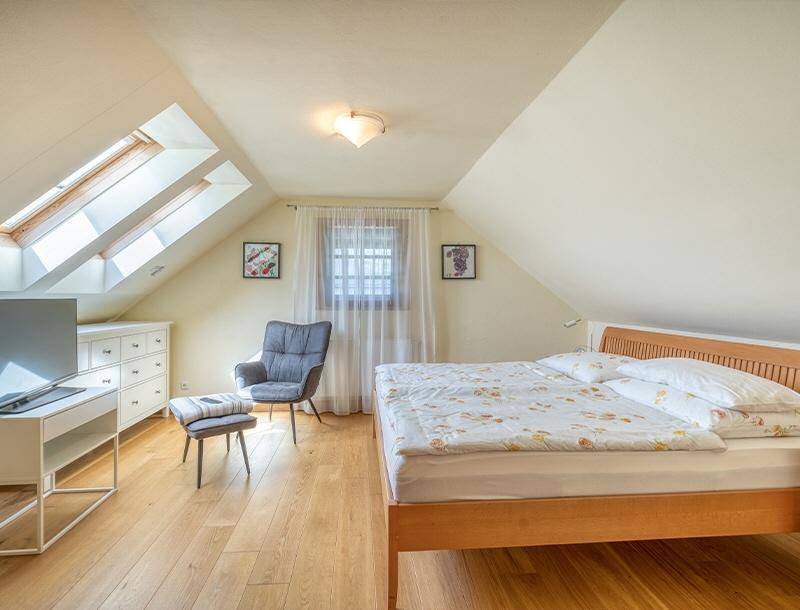 Helles Schlafzimmer im Dachgeschoss mit Holzboden, mehreren Dachfenstern und moderner Einrichtung.