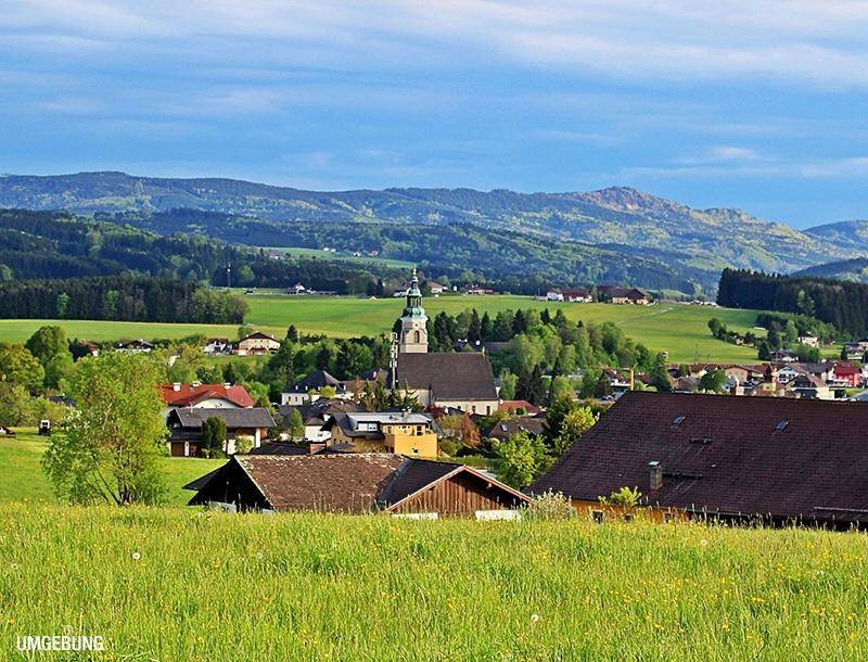 Malerische Weitblickaufnahme eines charmanten Dorfes mit Kirche, umgeben von grünen Hügeln und Feldern.