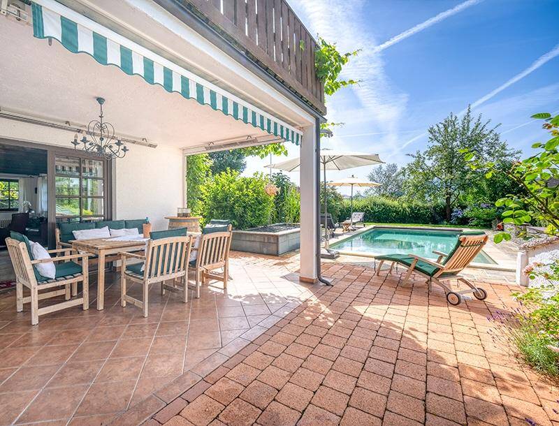 Großzügige Sonnenterrasse mit Markise, Gartenmöbeln und direktem Zugang zum privaten Pool.