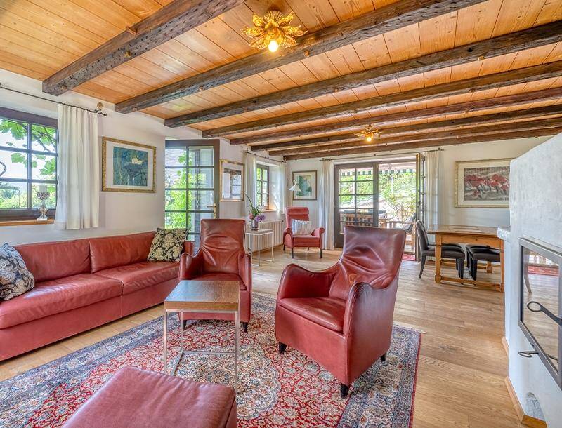 Gemütliches Wohnzimmer mit roten Ledermöbeln, traditionellem Kamin und rustikaler Holzbalkendecke.