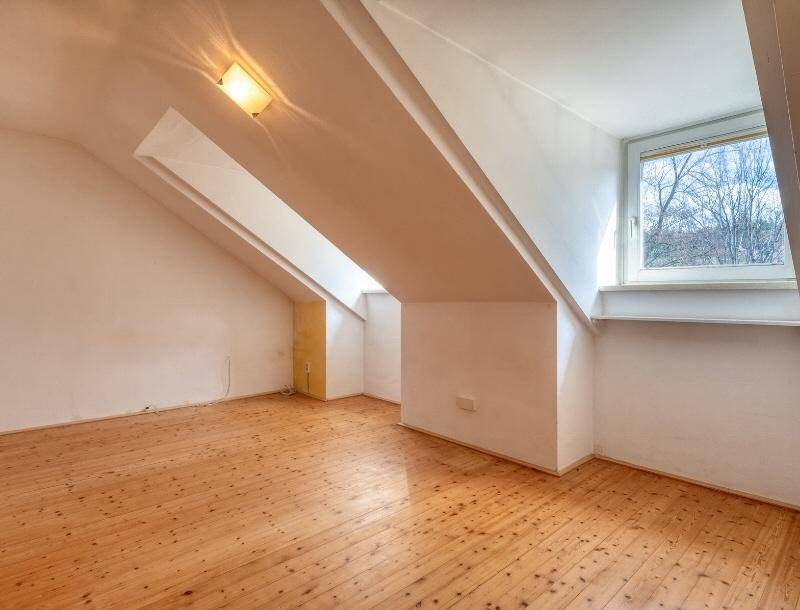 Dachgeschosszimmer mit Holzdielenboden und schrägen Wänden, hell durch das Fenster.
