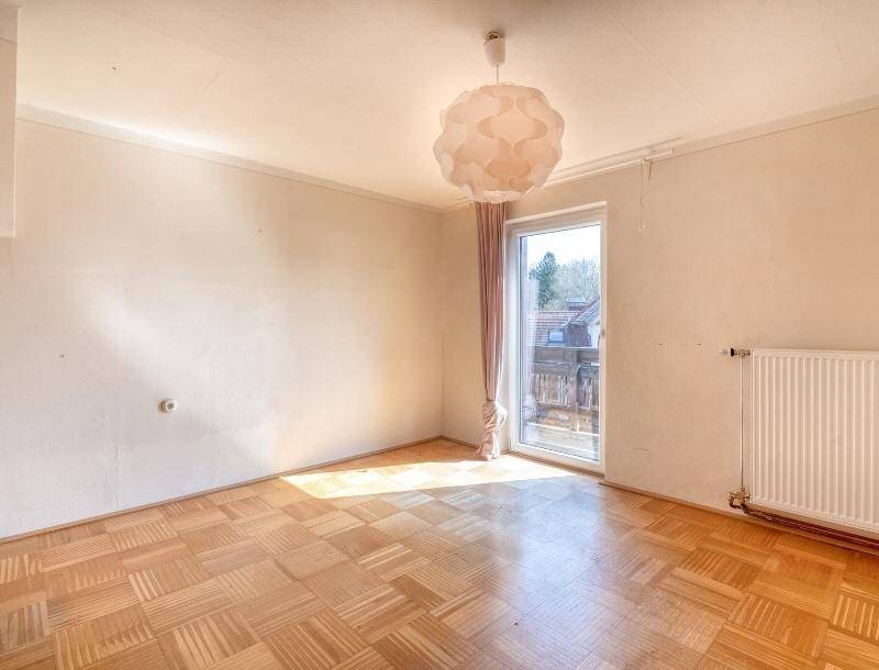 Helles Zimmer mit Parkettboden, Heizkörper und Zugang zu einem Außenbereich.
