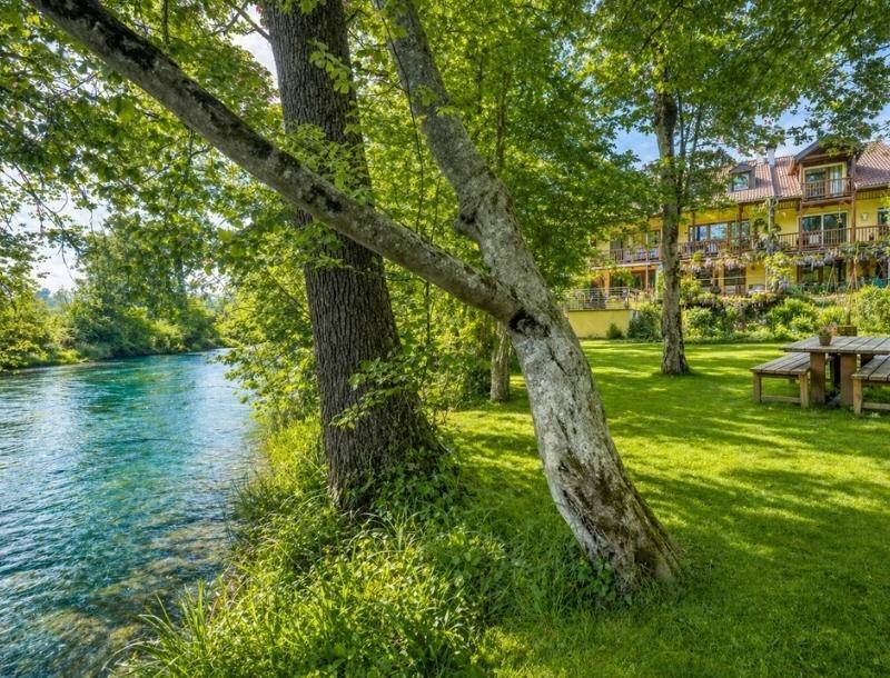 Idyllische Flusslandschaft mit klarem Wasser, umgeben von üppigem Grün und hohen Bäumen, nahe dem Anwesen.
