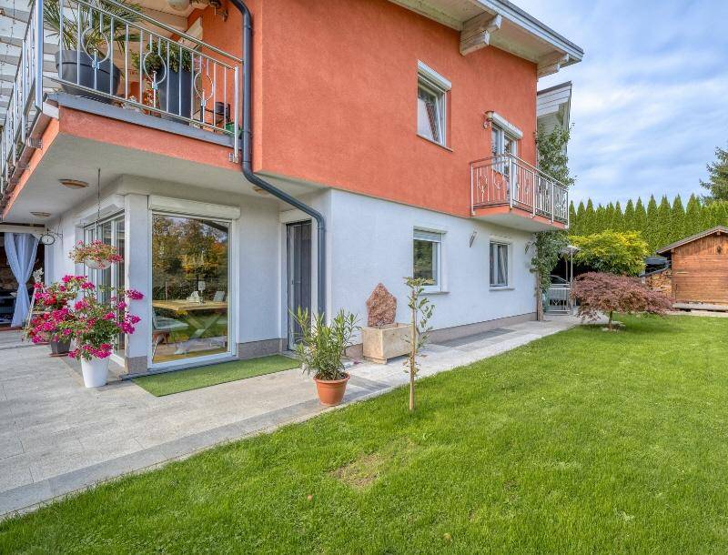 Seitenansicht des Hauses mit Zugang zum Garten, Balkonen und einem kleinen Gartenhaus im Hintergrund.