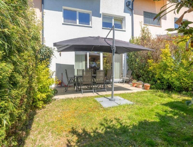 Gemütlicher Gartenbereich mit Rasenfläche und möblierter Terrasse unter einem Sonnenschirm.