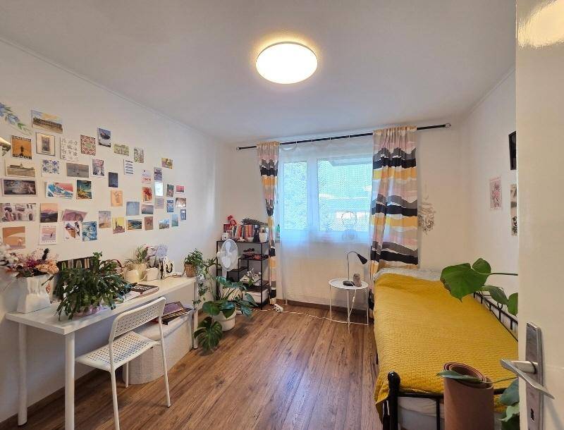 Helles Schlafzimmer mit Holzboden, Schreibtisch, vielen Pflanzen und persönlicher Wanddekoration.