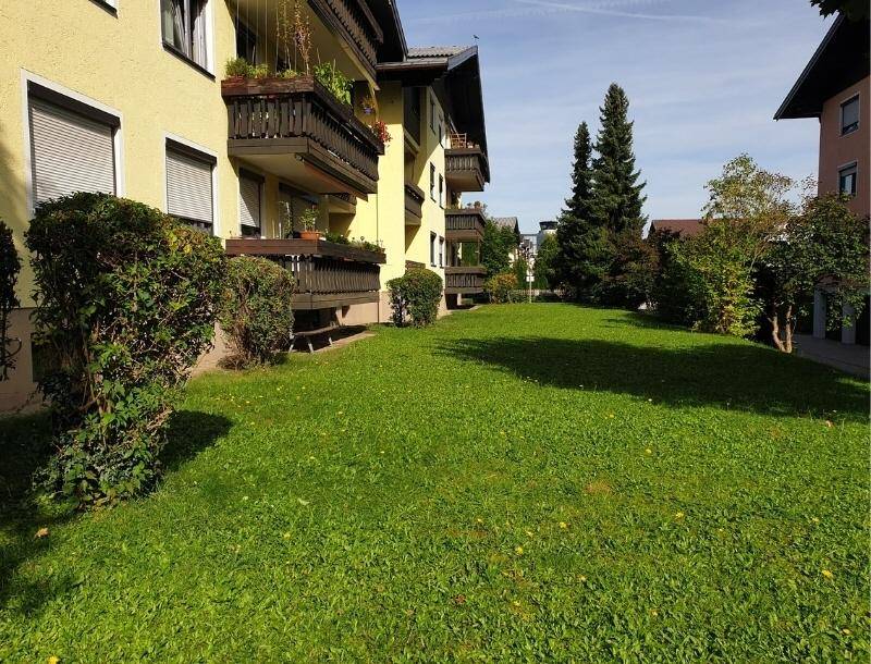 Gepflegte Rasenfläche vor einem Wohngebäude mit Balkonen und grüner Bepflanzung.
